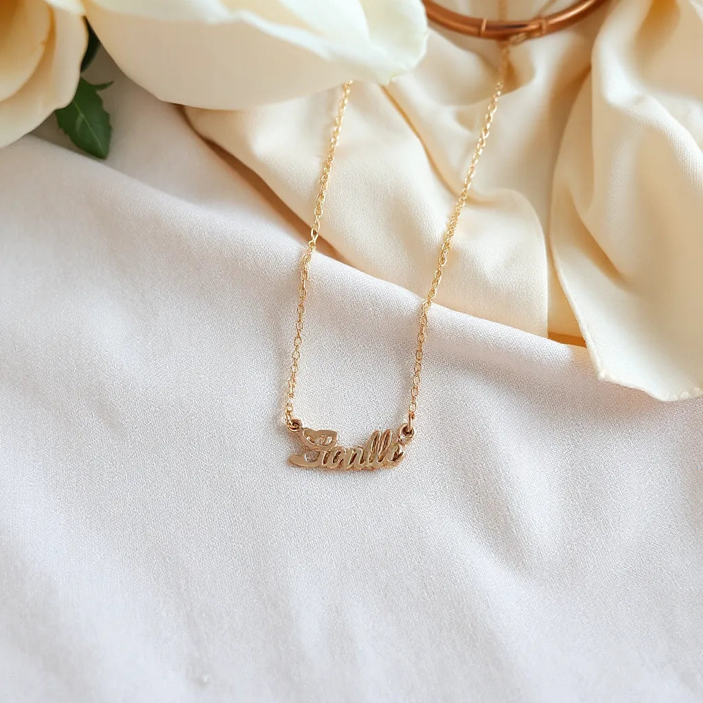 Delicate personalized name necklace pendant shown on a neutral fabric with minimal layered accessories