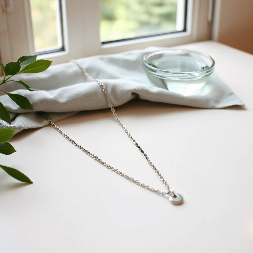 Polished stainless steel necklace with a microfiber cloth and water bowl on a clean light background