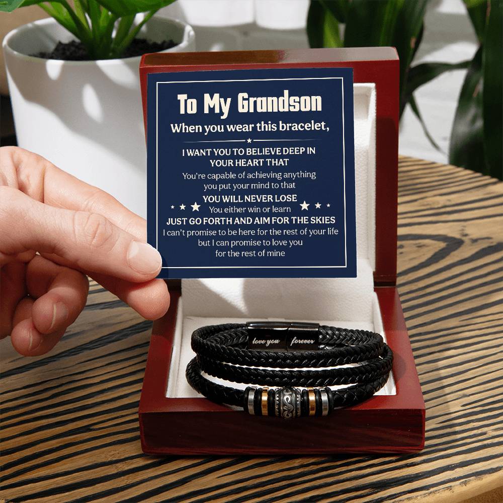 A hand holding a black leather love you forever bracelet for grandson with a heartfelt note in a box.