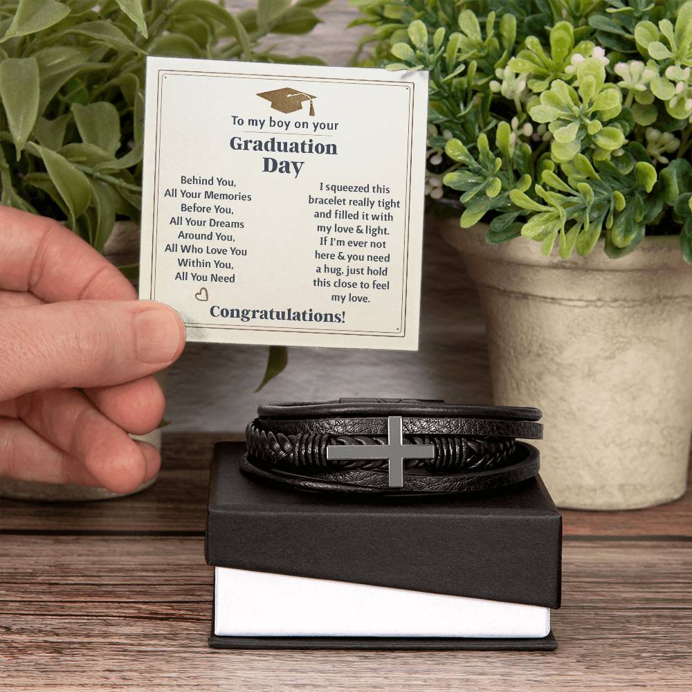 Hand holding a heartfelt graduation card next to a men's cross bracelet graduation gift in a gift box.