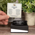 Hand holding a heartfelt graduation card next to a men's cross bracelet graduation gift in a gift box.