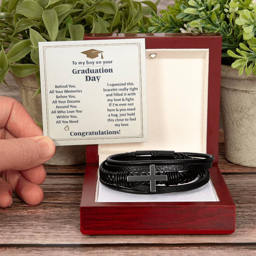 Hand holding a black cross bracelet graduation gift in a wooden box with a heartfelt graduation message card.