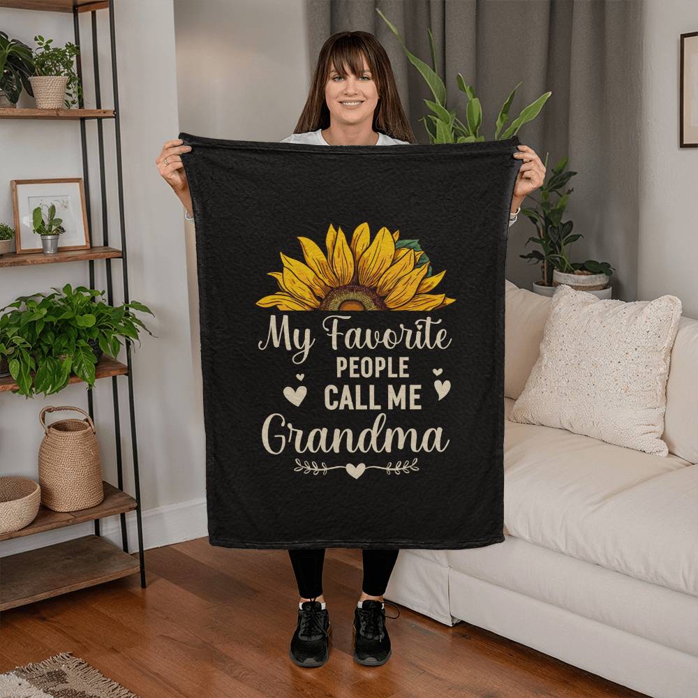 Woman holding a coral fleece blanket with 'My Favorite People Call Me Grandma' and a sunflower design.