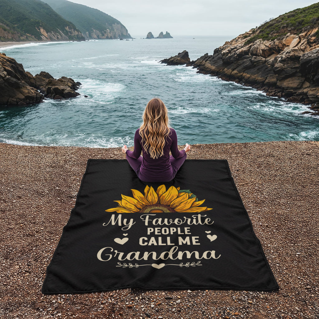 A woman sitting on a coral fleece blanket for grandma by the ocean, enjoying nature and comfort.