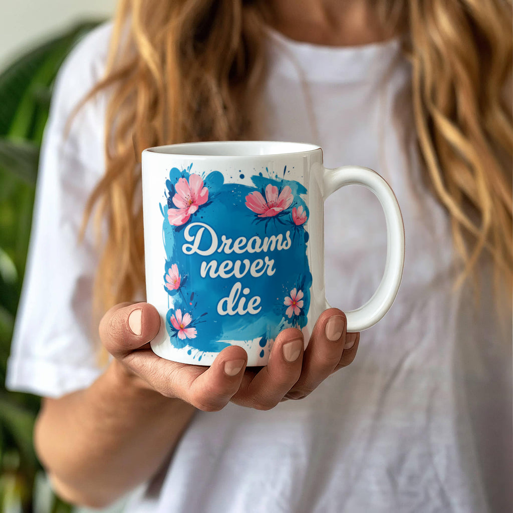 Dreams Never Die 11oz White Ceramic Motivational Coffee Mug held by a person with floral design.