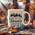 custom ceramic coffee mug with mountain design and text 'And so the Adventure begins' on a wooden surface.