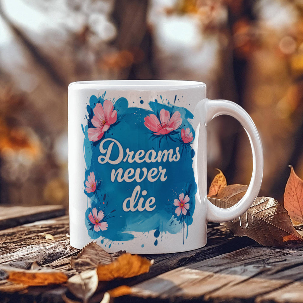 Dreams Never Die 11oz White Ceramic Motivational Coffee Mug with floral design on a rustic table.